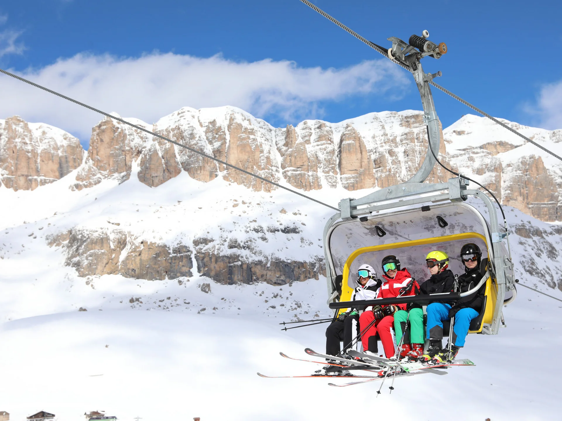 Il tuo Chalet ad Arabba: Chalet Barbara, charme alpino. Quattro sciatori su seggiovia con montagne innevate sullo sfondo