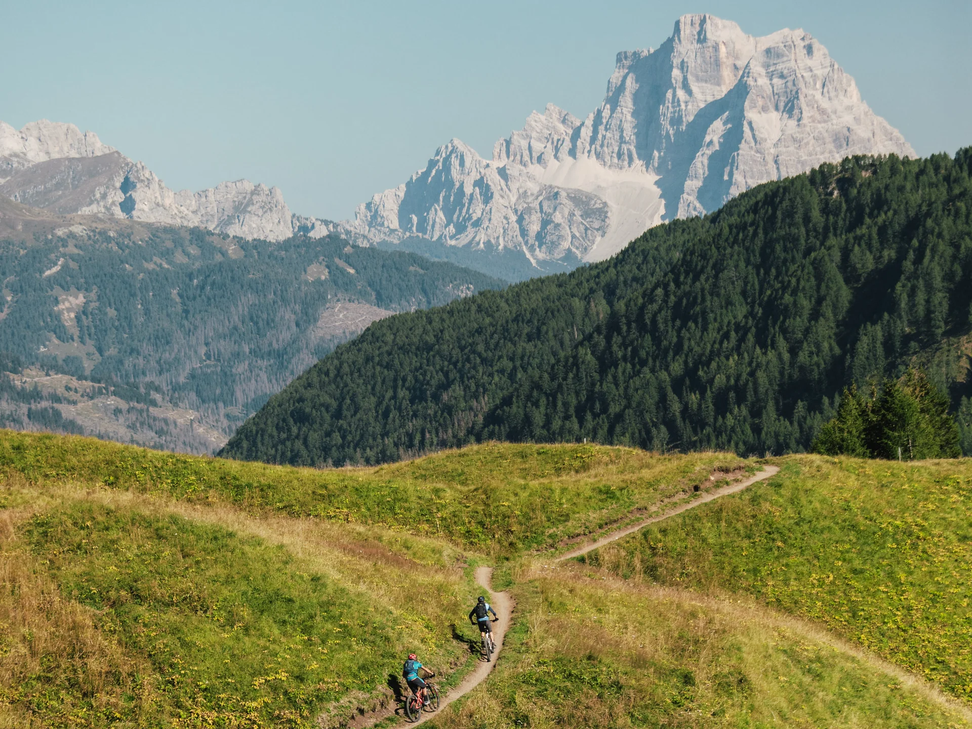 Il tuo Chalet ad Arabba: Chalet Barbara, charme alpino. Due ciclisti su sentiero in collina con montagne rocciose sullo sfondo