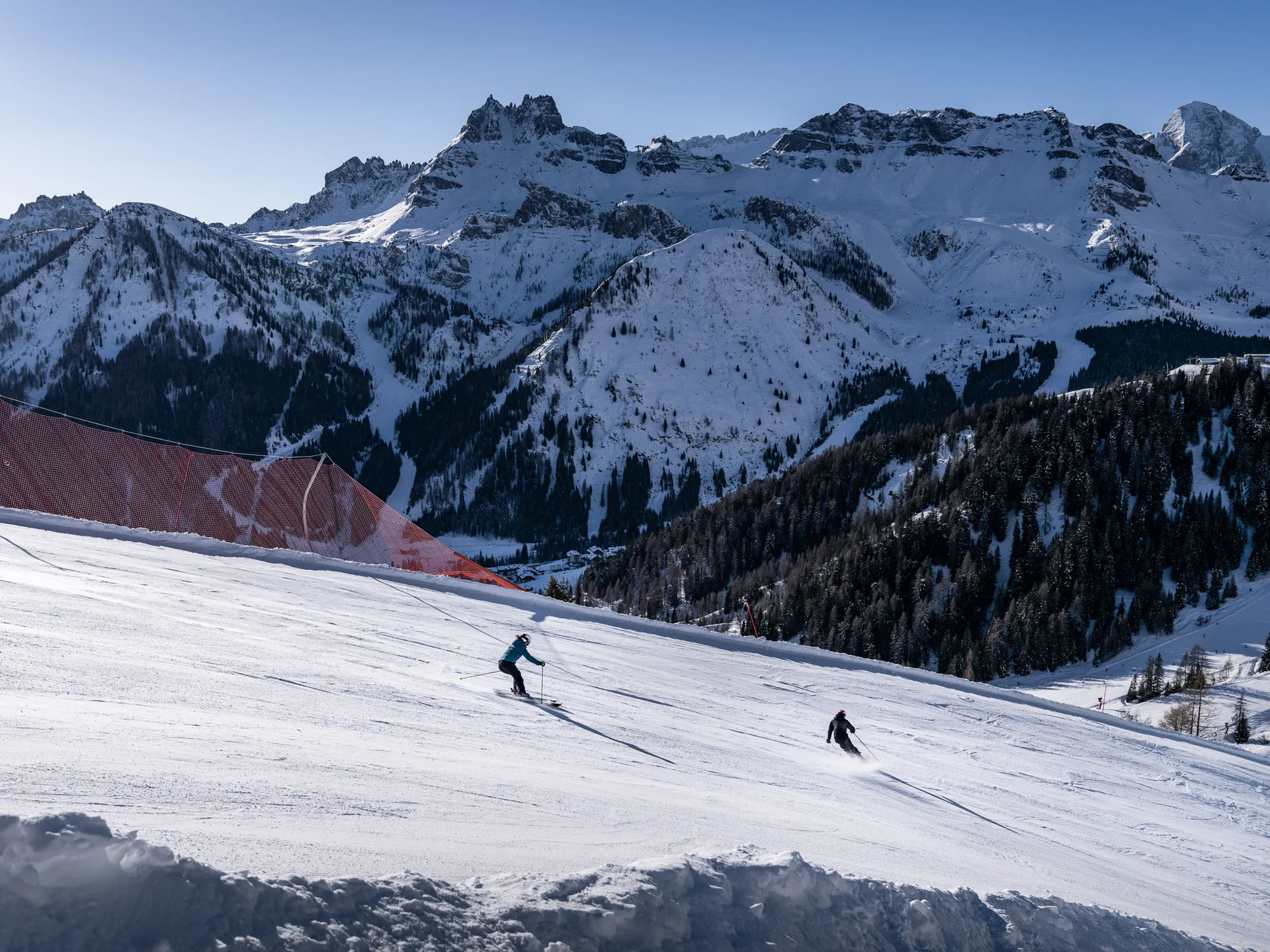 Il tuo Chalet ad Arabba: Chalet Barbara, charme alpino. Sciatori che scendono una pista innevata con montagne innevate sullo sfondo