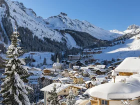 Il tuo Chalet ad Arabba: Chalet Barbara, charme alpino. Paesino innevato tra le montagne con alberi e case sotto il cielo azzurro