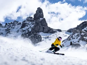 Il tuo Chalet ad Arabba: Chalet Barbara, charme alpino. Sciatore con giacca gialla sulle piste innevate con montagne rocciose sullo sfondo