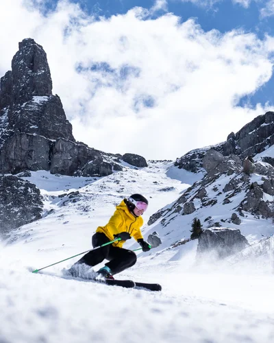 Il tuo Chalet ad Arabba: Chalet Barbara, charme alpino. Sciatore con giacca gialla sulle piste innevate con montagne rocciose sullo sfondo