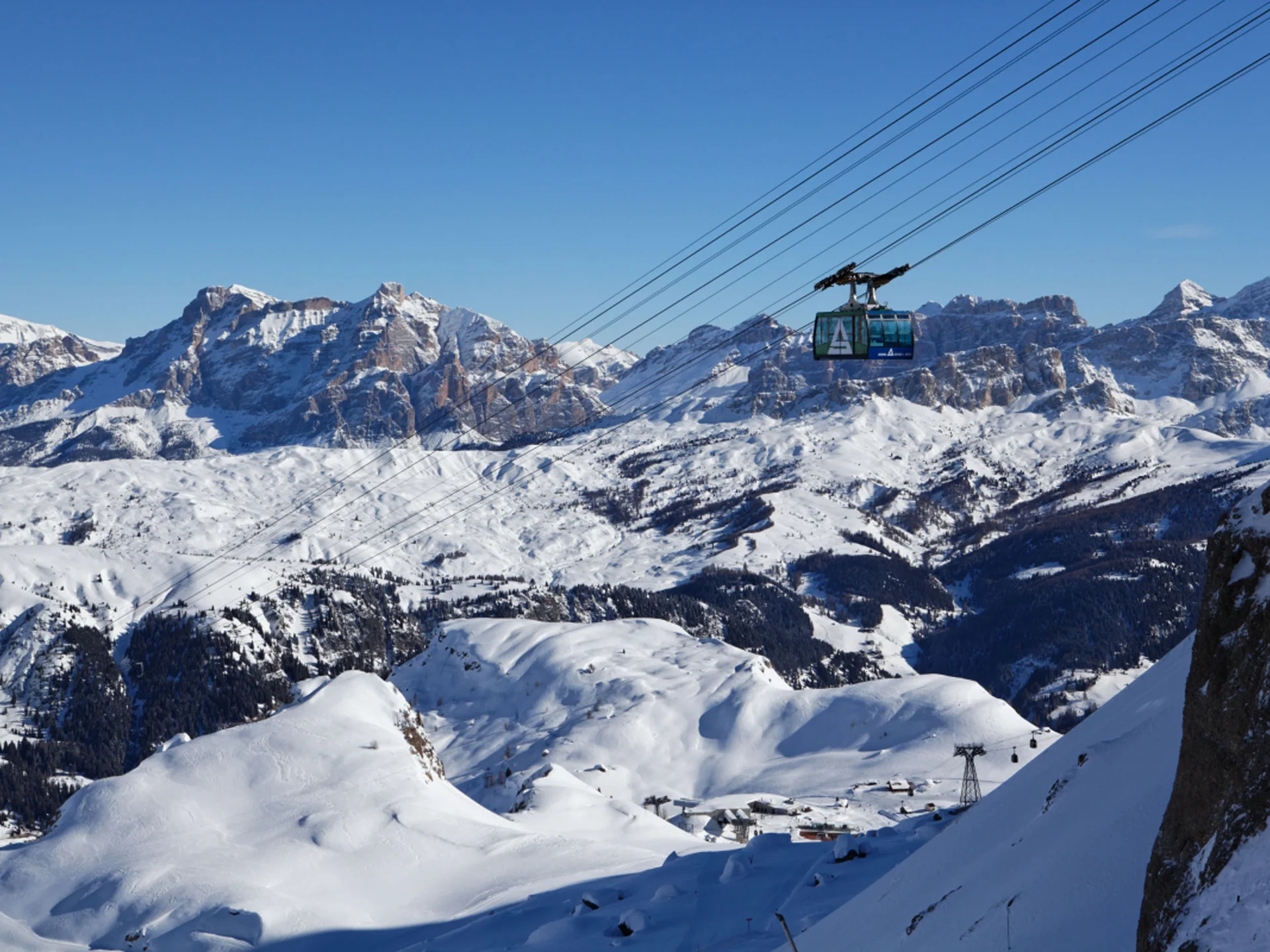 Il tuo Chalet ad Arabba: Chalet Barbara, charme alpino. Funivia che attraversa montagne innevate con cielo azzurro limpido